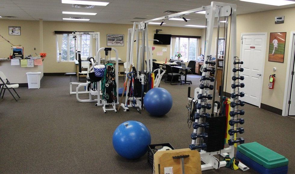 Inside a physical therapy clinic: exercise equipment, blue stability balls, and weights on racks.