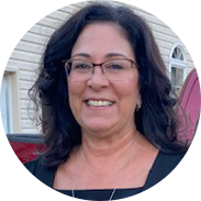 Woman with glasses smiling, dark hair, wearing a black top, outdoors in front of a building.