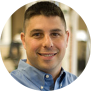 Man with short dark hair, smiling, wearing a blue button-down shirt.