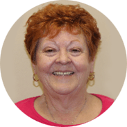 Woman with short red hair and a pink shirt smiles at the camera.