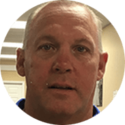 Man with short hair and light eyes looking at the viewer. He wears a blue shirt.