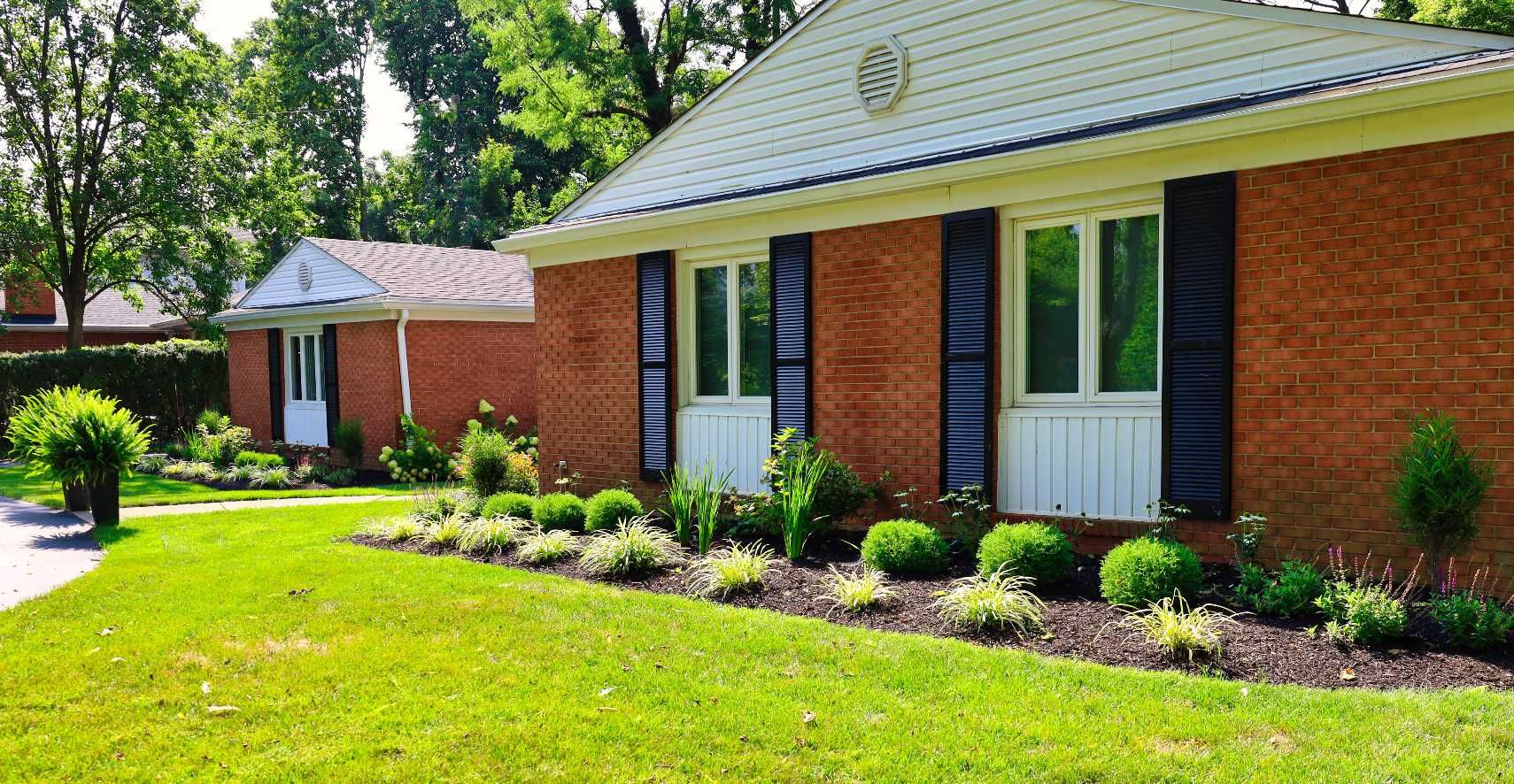 A brick house with white shutters and a lush green lawn in front of it.