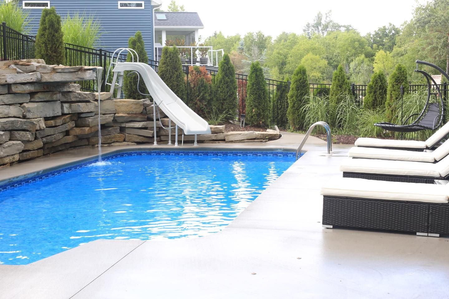 A large swimming pool with a slide and chairs around it.