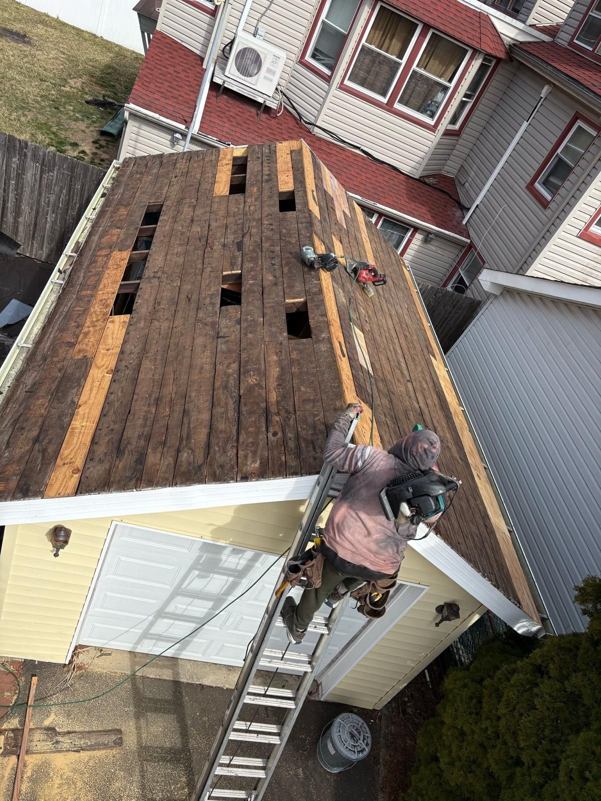 A man is standing on a ladder on the roof of a house.