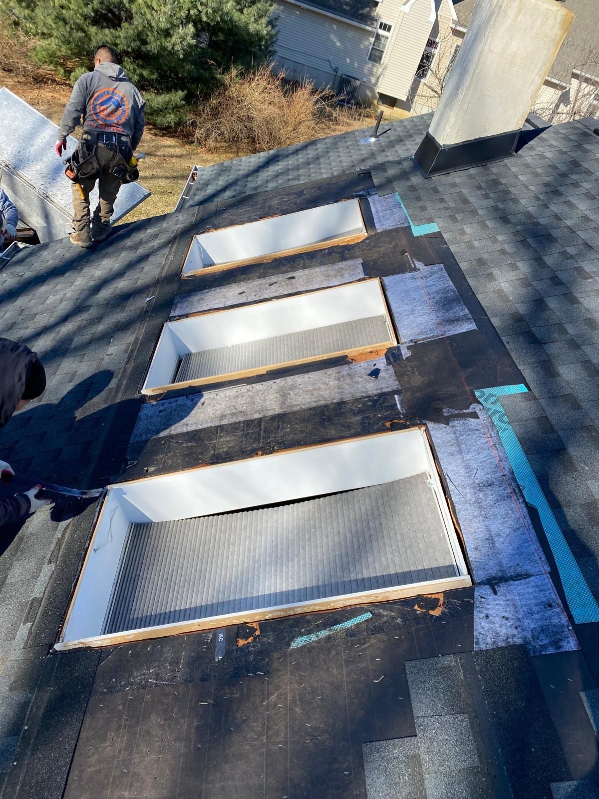 A man is standing on top of a roof with a row of skylights.