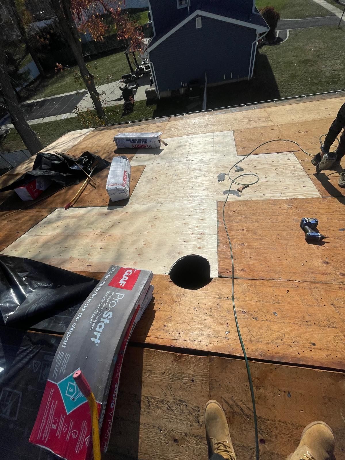 A person is standing on a roof with a box of roofing material in the foreground.