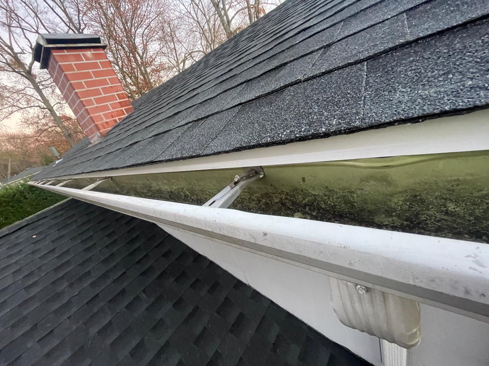 A gutter on the side of a house with a chimney on the roof.