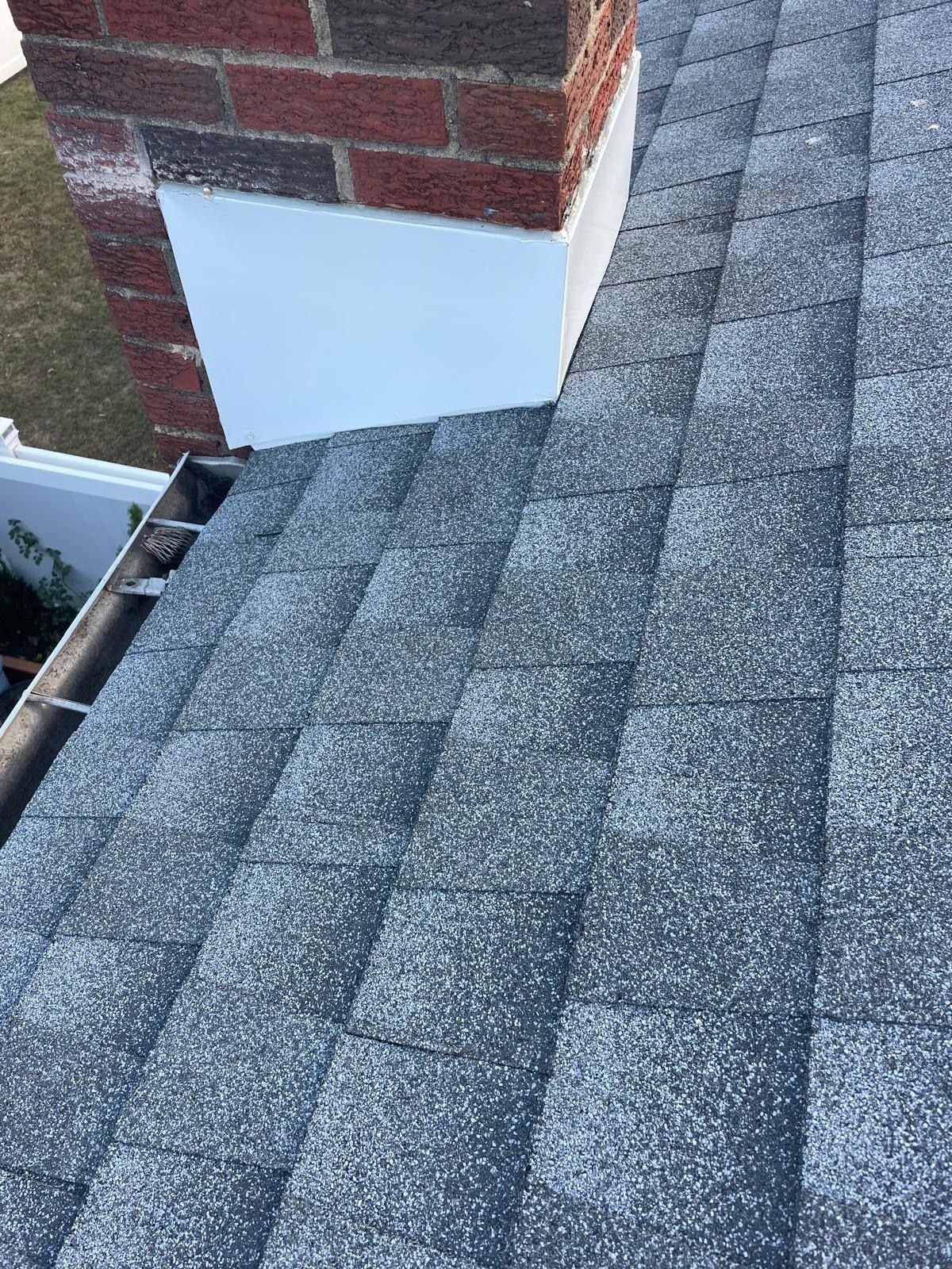 A close up of a roof with a chimney in the background.