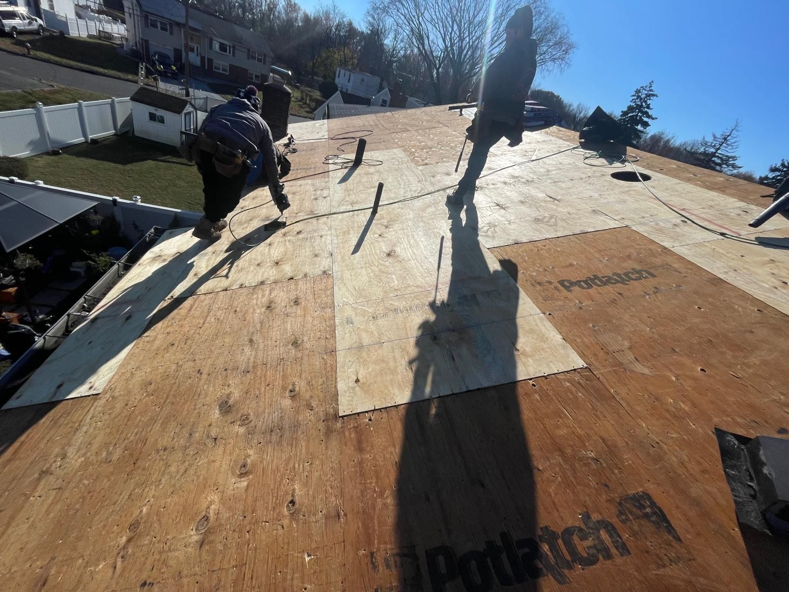 A man is working on a roof with a sheet of plywood that says potlatch on it