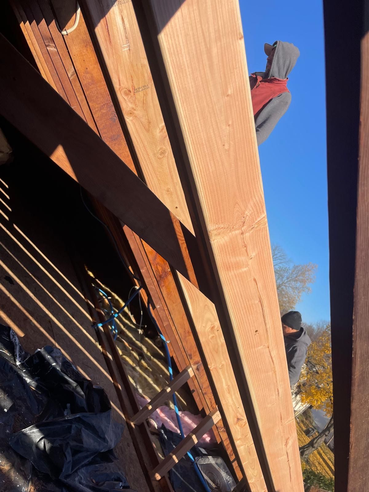 A person is sitting on a wooden beam looking up at the sky