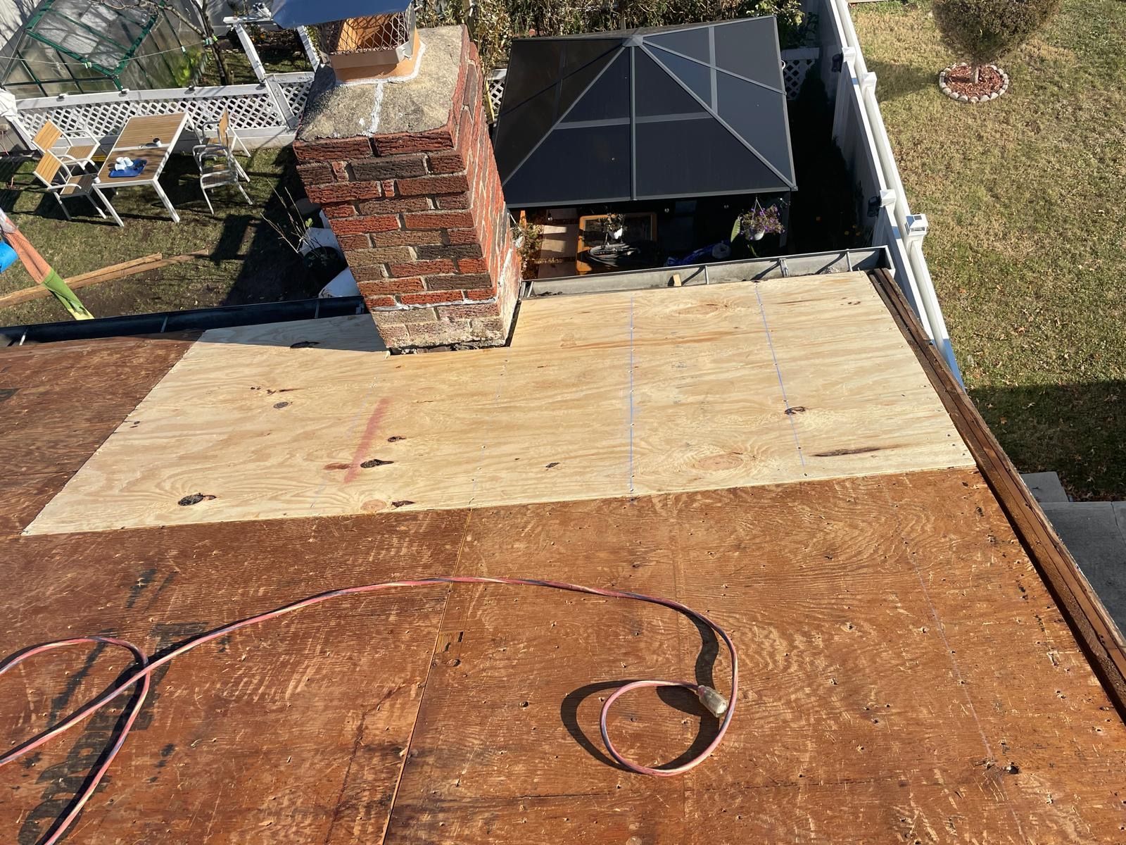 An aerial view of a roof with a brick chimney and plywood on it.