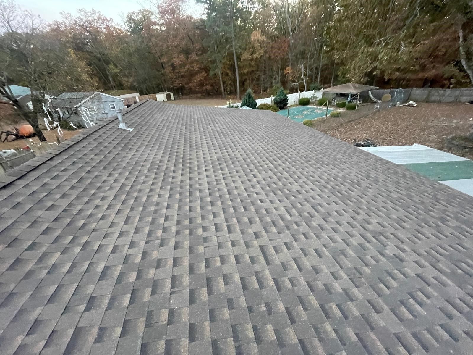 The roof of a house with a pool and trees in the background.
