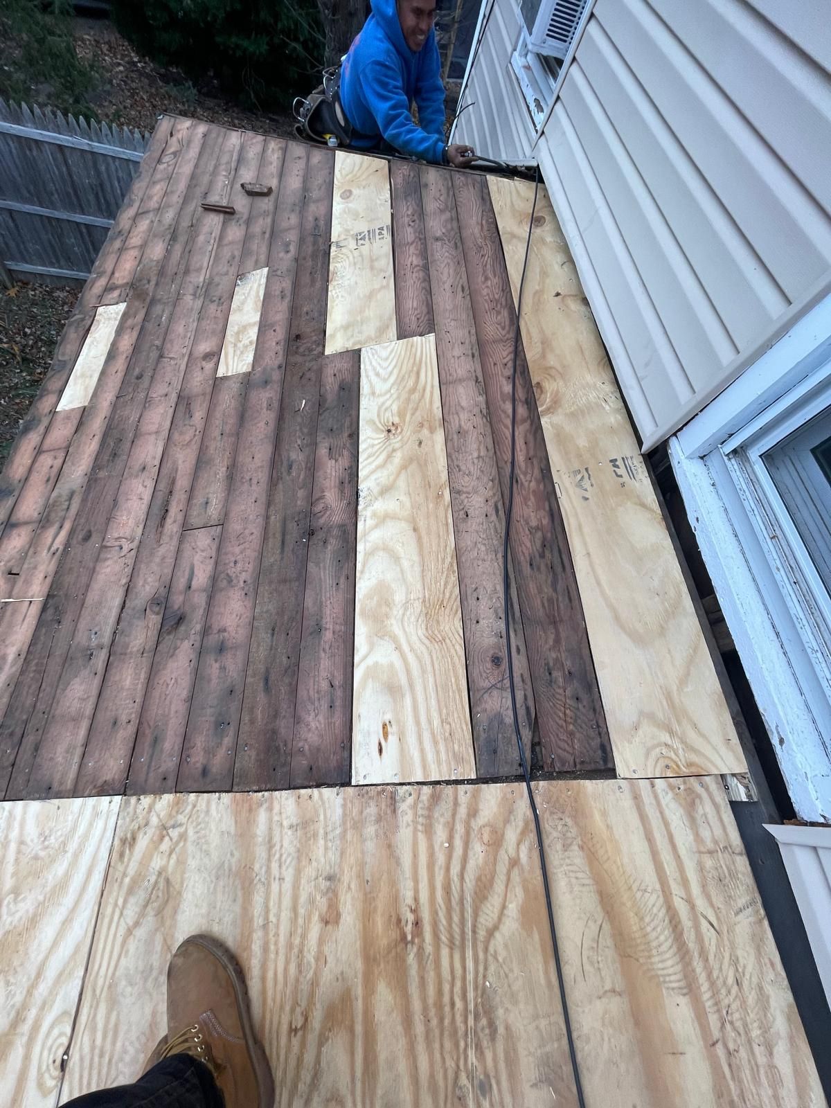 A man is working on a wooden deck next to a house.