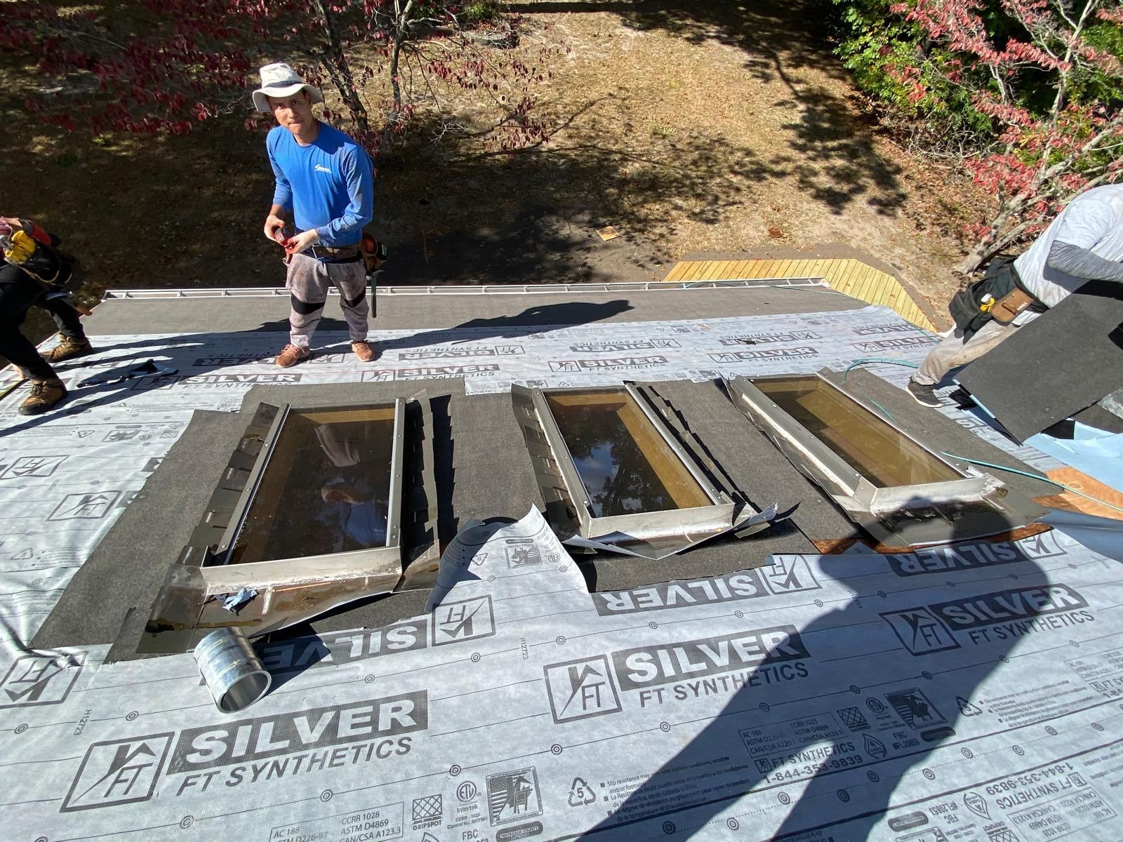 A man is standing on top of a roof with a bunch of windows on it.