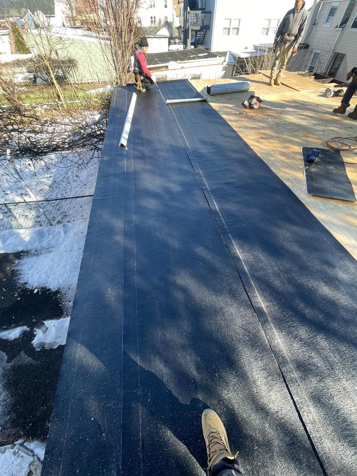 A person is standing on top of a black roof.