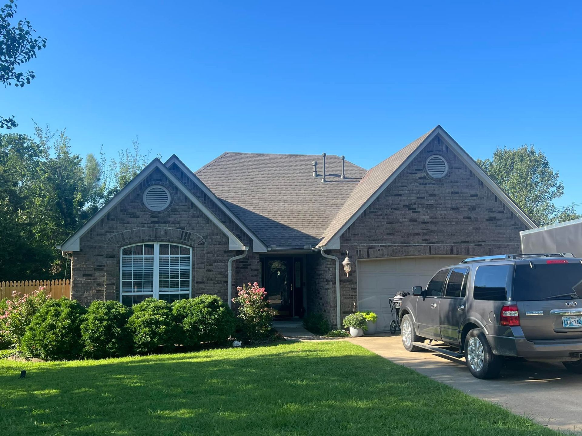 Brick house with gray roof, blue sky, green lawn, and SUV in the driveway.