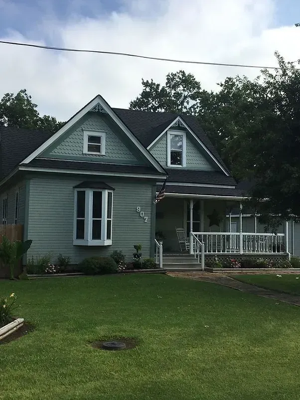 Green house with a porch, bay window, and dormers, on a grassy lawn.