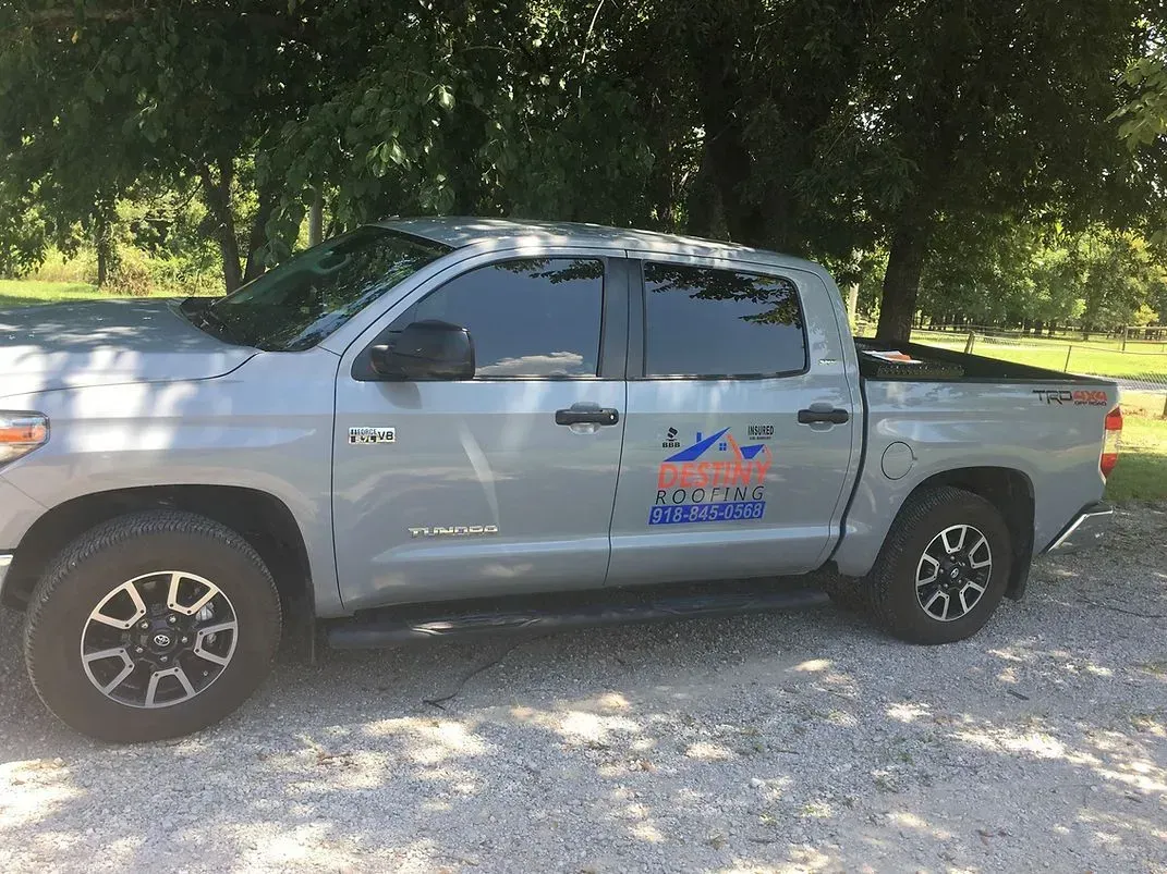 Gray Toyota Tundra pickup truck parked under a tree, with business logo on the side.