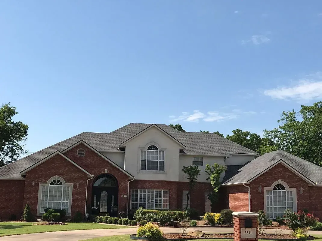 Brick and stucco house under a blue sky, with tile roof and arched windows.