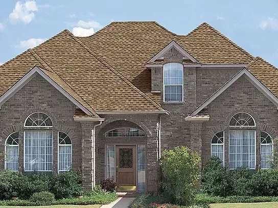 Brick house with brown roof, arched windows, and front door, blue sky background.