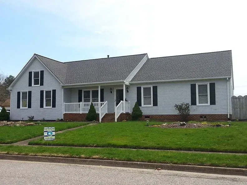 Light blue house with black shutters, a white porch, and a green lawn.