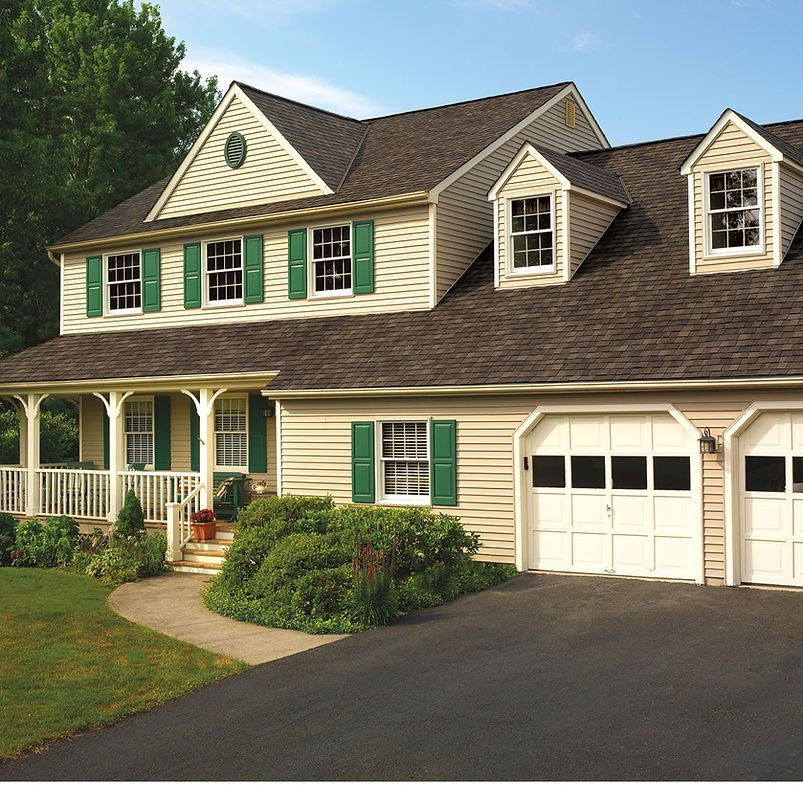 Two-story beige house with green shutters, a porch, and a driveway.
