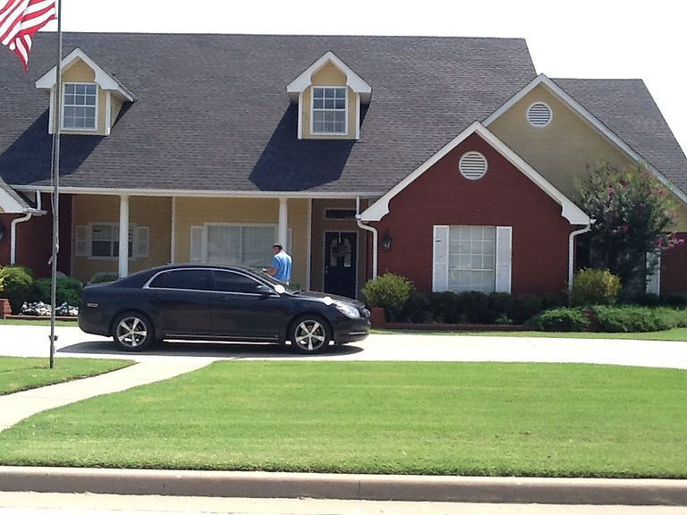Black car parked in front of a large house with a red and yellow exterior; person by the front door.