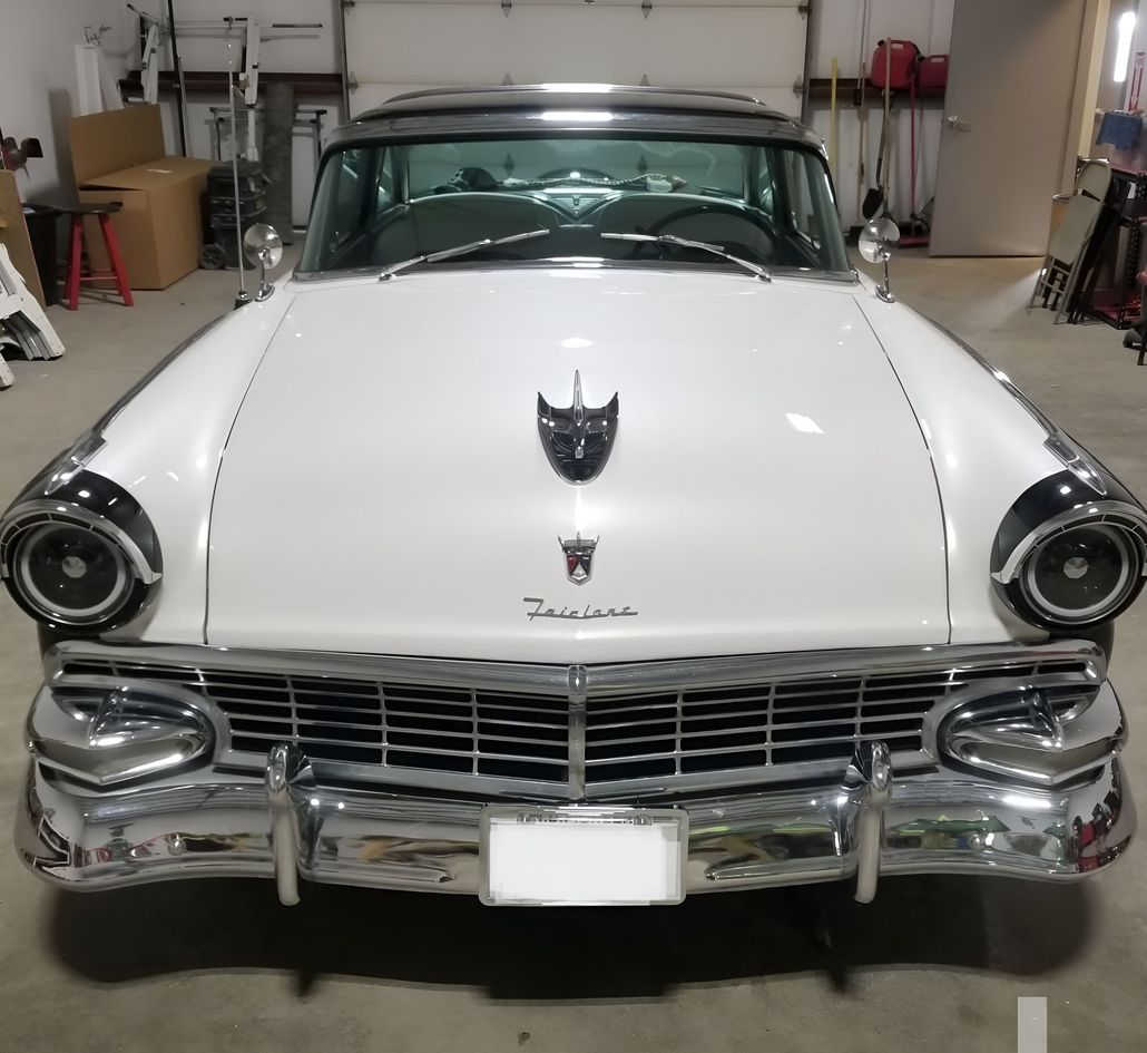 White and black vintage Ford Fairlane car in a garage, front view. Chrome bumper, headlights, and grill.