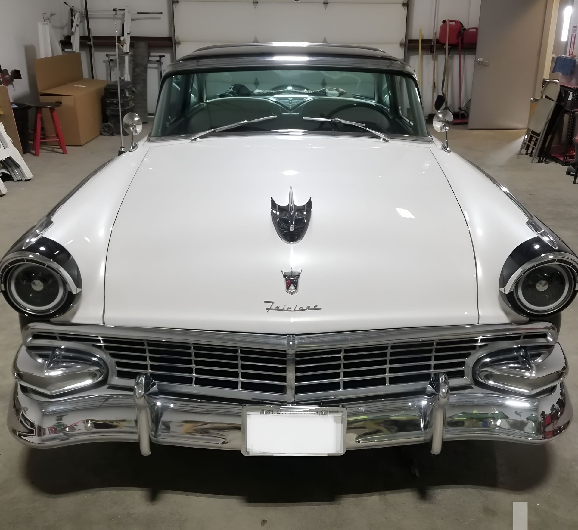 White and black vintage Ford Fairlane car in a garage, front view. Chrome bumper, headlights, and grill.