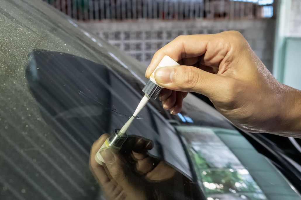 Person applying liquid sealant to a car windshield, garage setting.