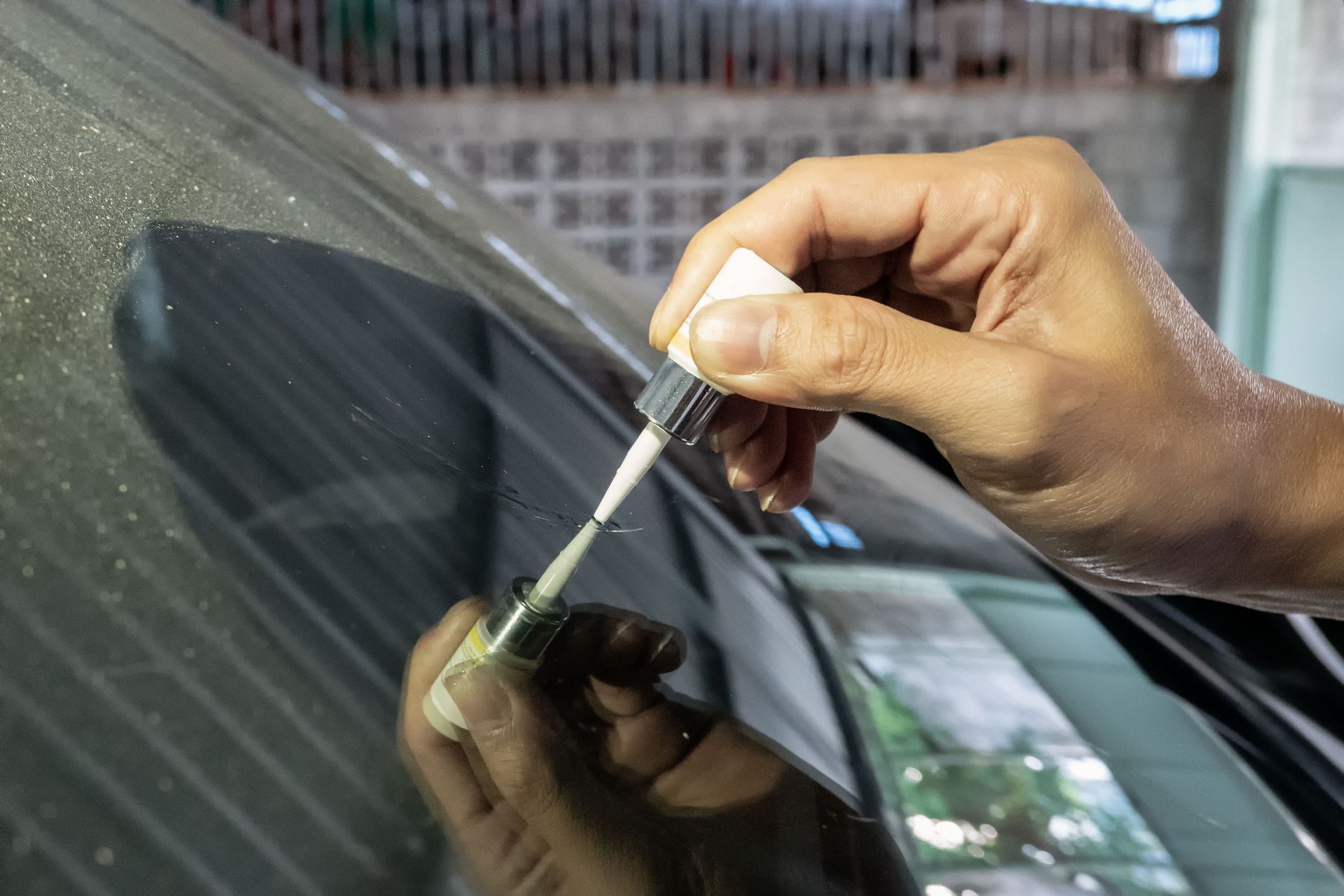 Person applying liquid sealant to a car windshield, garage setting.