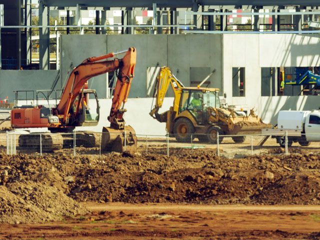 Construction site with orange excavator and yellow backhoe operating near a partially built building.