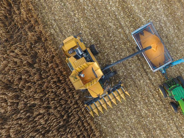 Aerial view: Yellow combine harvesting grain, unloading into a trailer, alongside a green tractor in a field.