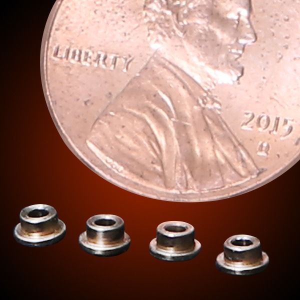Four small metal bushings beside a US penny for size comparison.