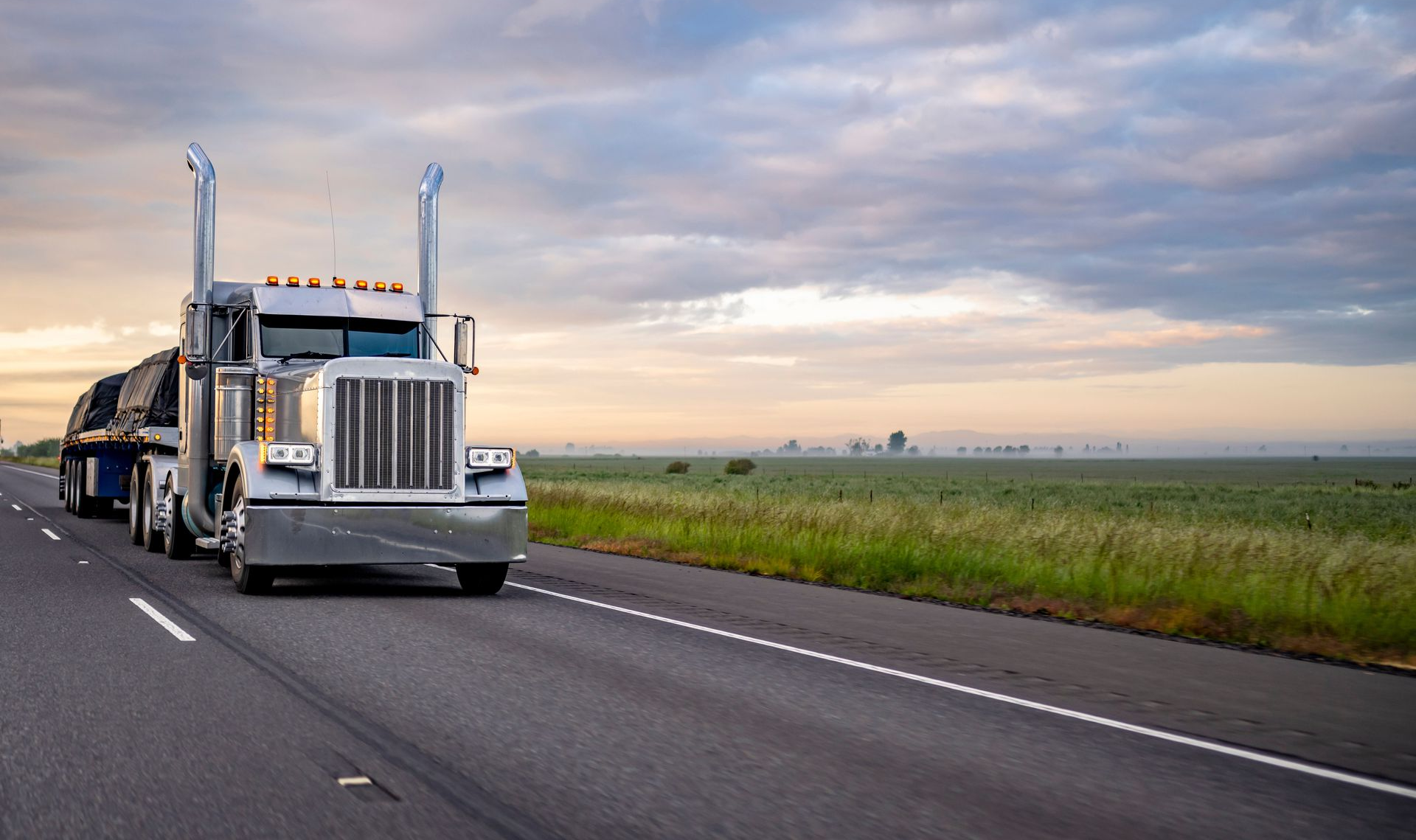 Semi-truck hauling cargo on a highway under a cloudy sky.