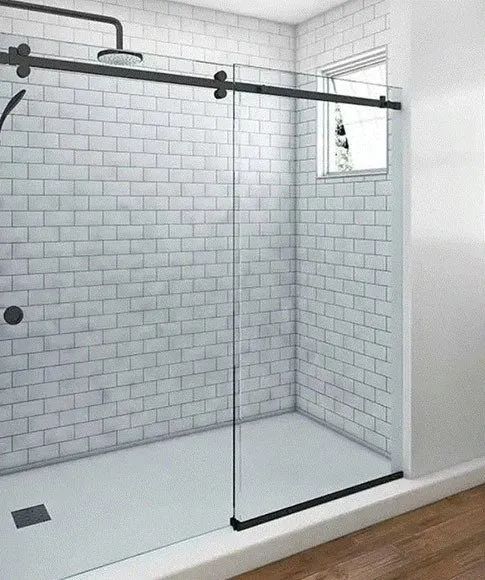 A glass shower enclosure with a black sliding track and frame, set against white subway tile walls.