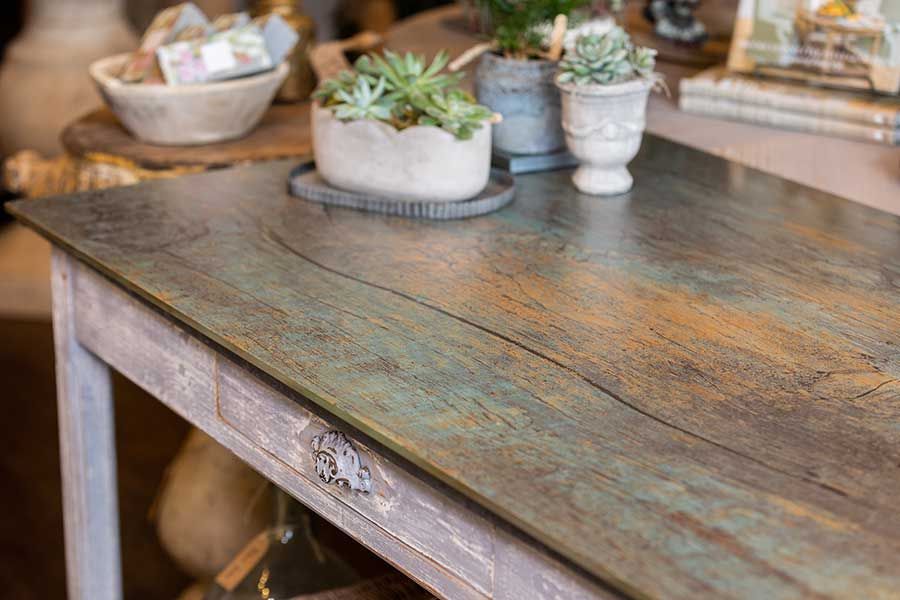 A rustic wooden table with a distressed, teal-toned top, featuring potted succulents and a bowl of items on its surface.