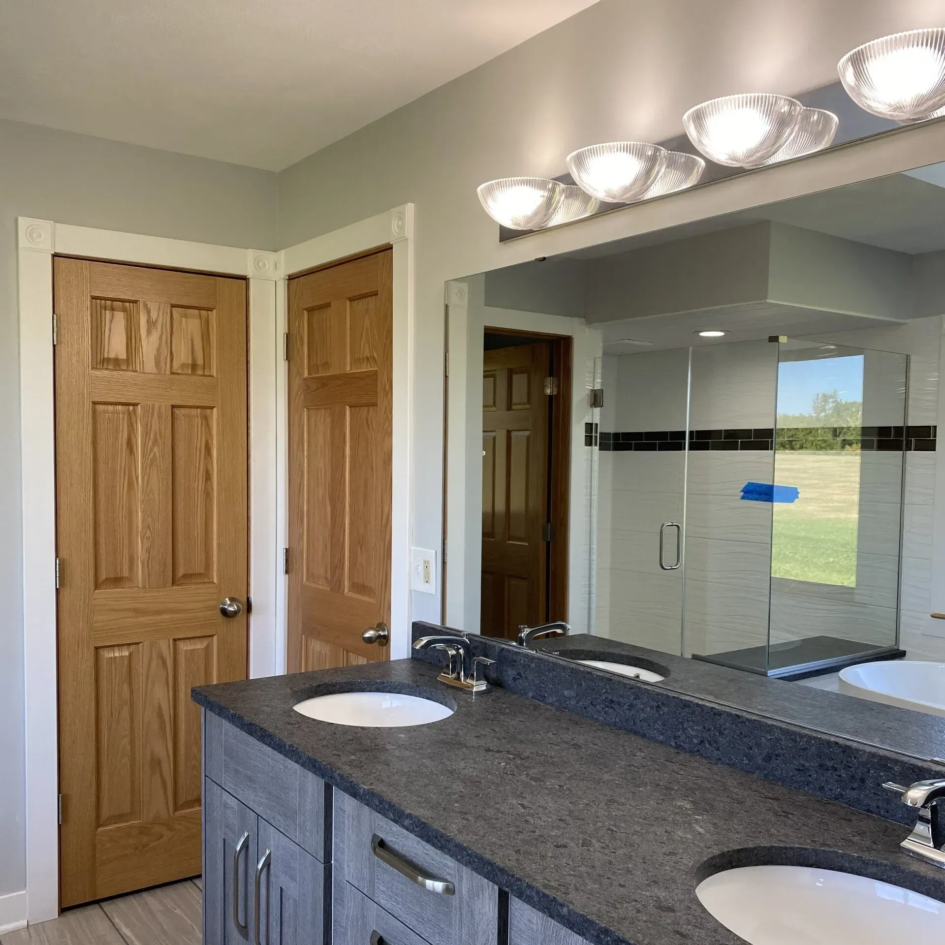 A modern bathroom vanity with gray cabinets and dark stone countertops, featuring two sinks and a large mirror.