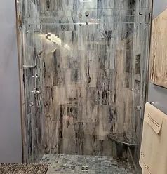 A modern walk-in shower with grey and white marbled tile walls, glass sliding doors, and a tiled seat.
