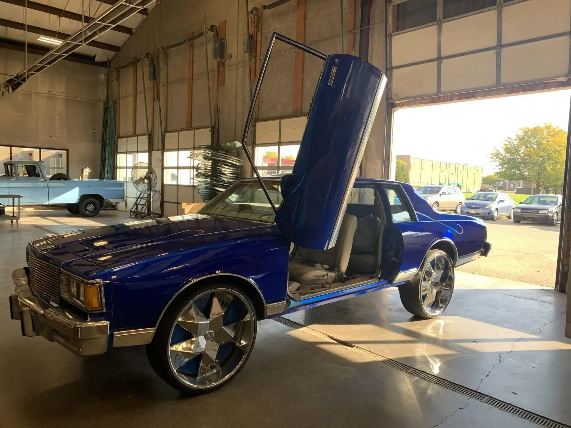 A metallic blue modified car with vertical doors and large custom wheels parked inside a garage.