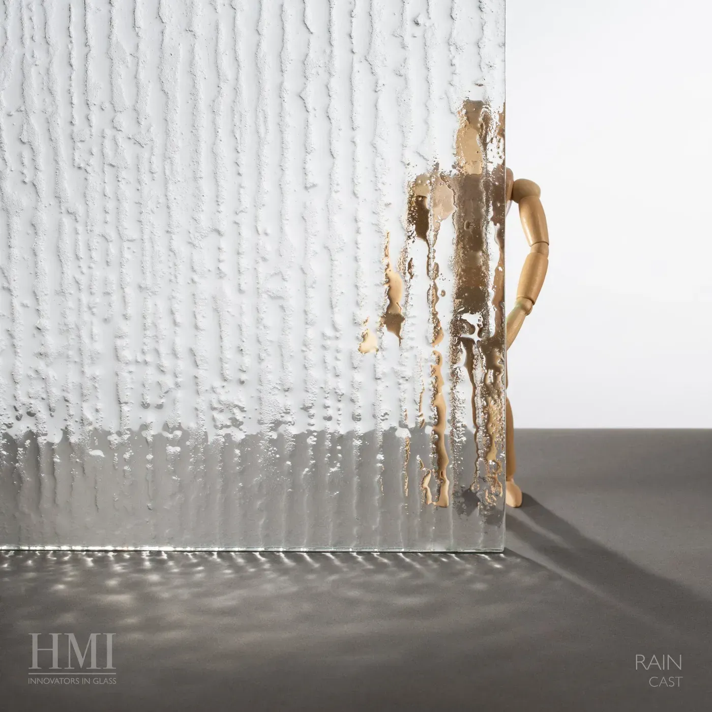 A piece of textured, vertical-patterned rain glass obscuring a wooden artist mannequin on a gray surface.