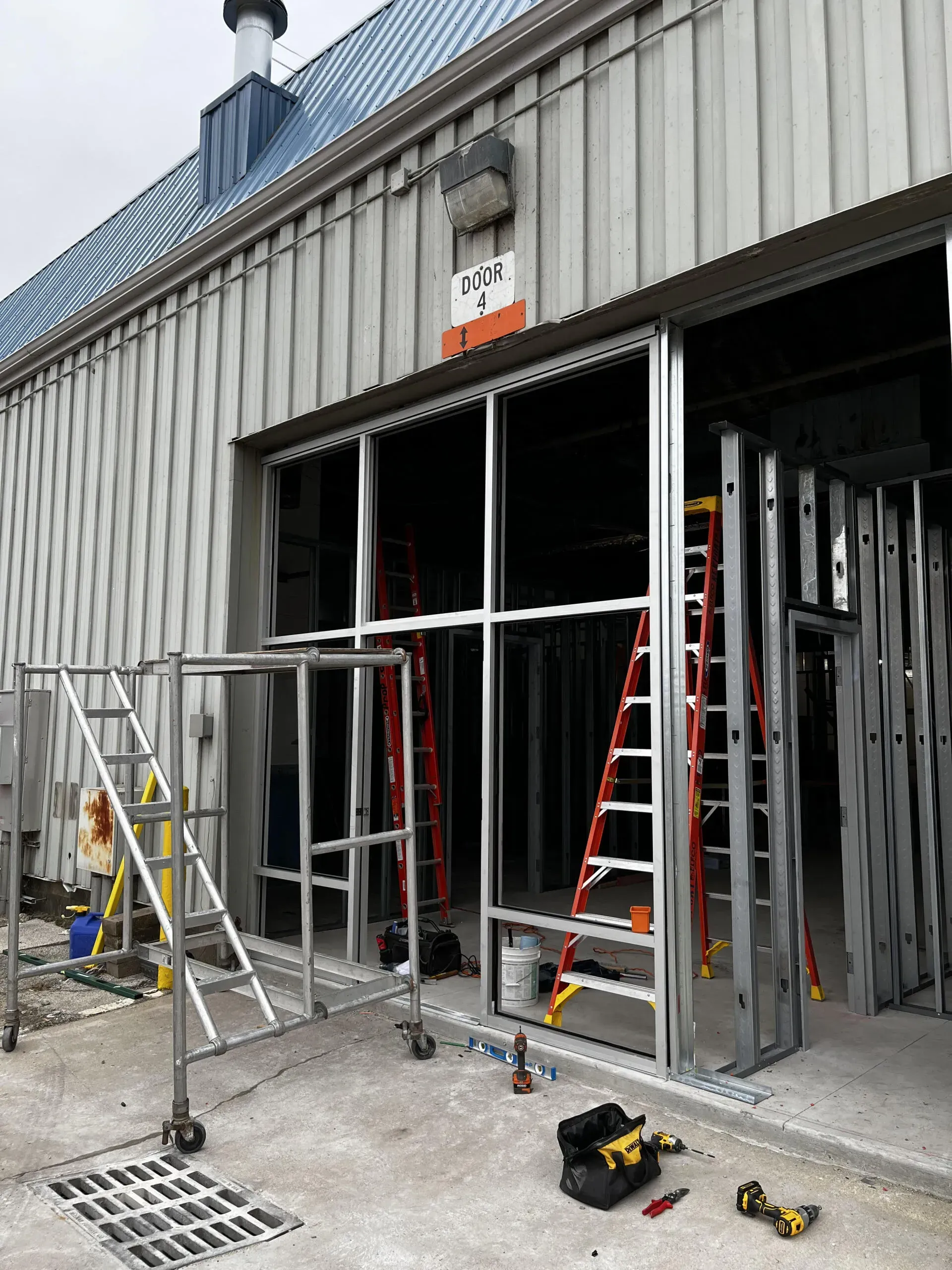 A commercial building exterior under construction with metal framing, ladders, scaffolding, and tools.
