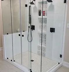A modern walk-in shower with a glass enclosure, black hardware, white tiled walls, and decorative patterned niches.