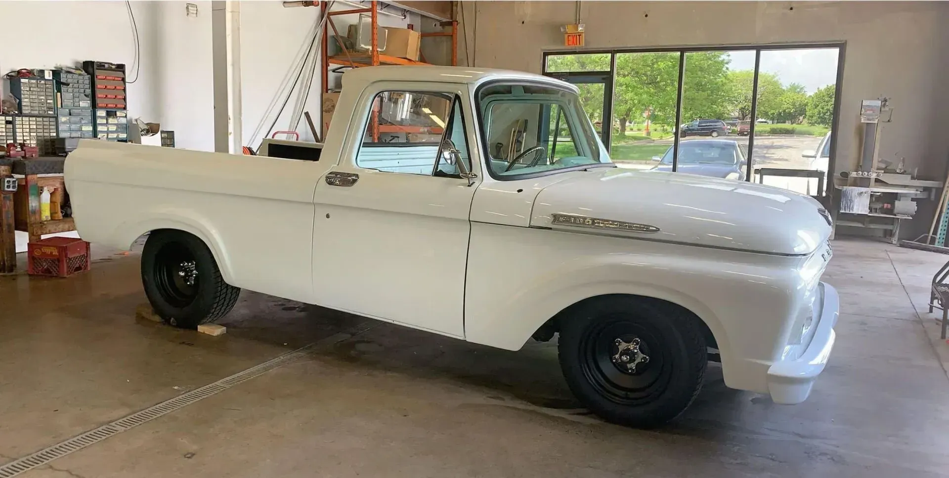 A white, vintage Ford F-series pickup truck parked inside a bright, spacious workshop.