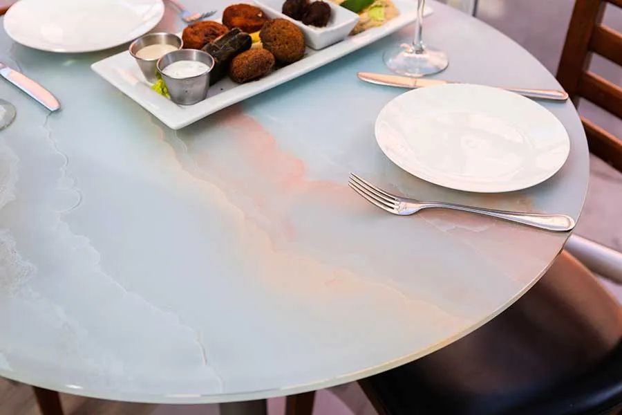 A round white table set with two plates, a fork, a butter knife, and a rectangular platter of appetizers and dips.