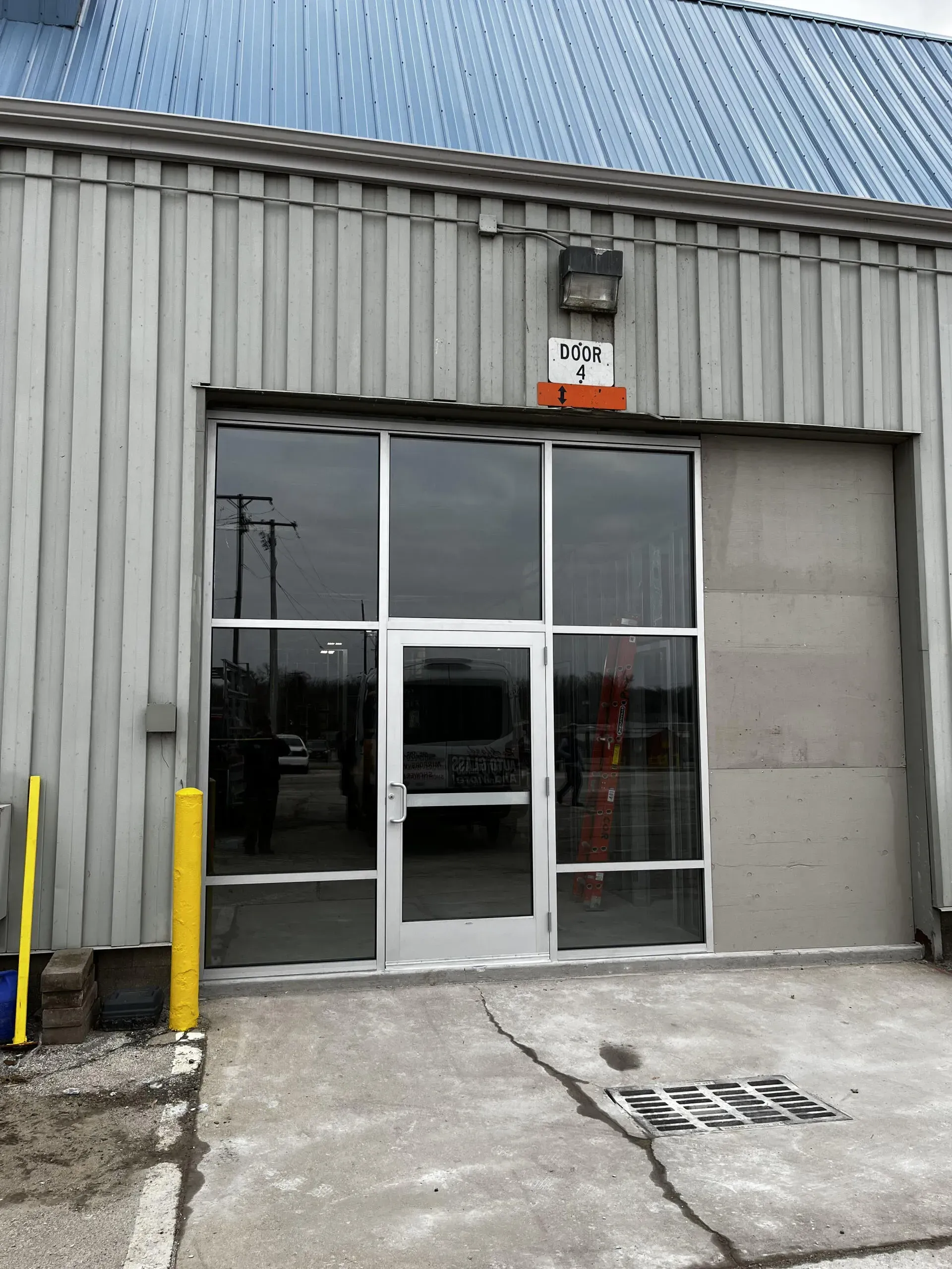 Entrance with a glass door and side panels set in a grey industrial metal building with a concrete floor.