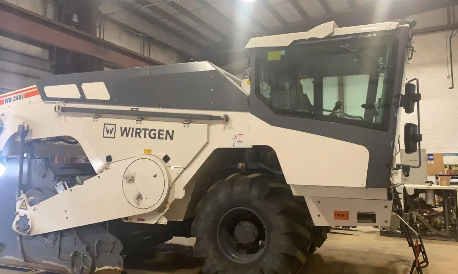 A white and gray Wirtgen road milling machine parked inside a large, industrial workshop.