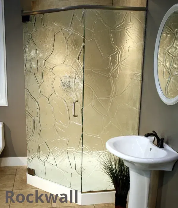 A modern corner shower with textured rock-patterned glass, next to a white pedestal sink in a neutral-toned bathroom.