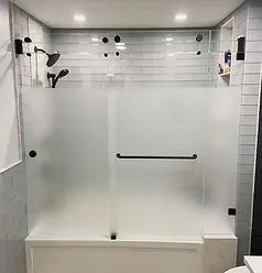 Frosted sliding glass shower doors over a white bathtub with black hardware against a white subway tile wall.