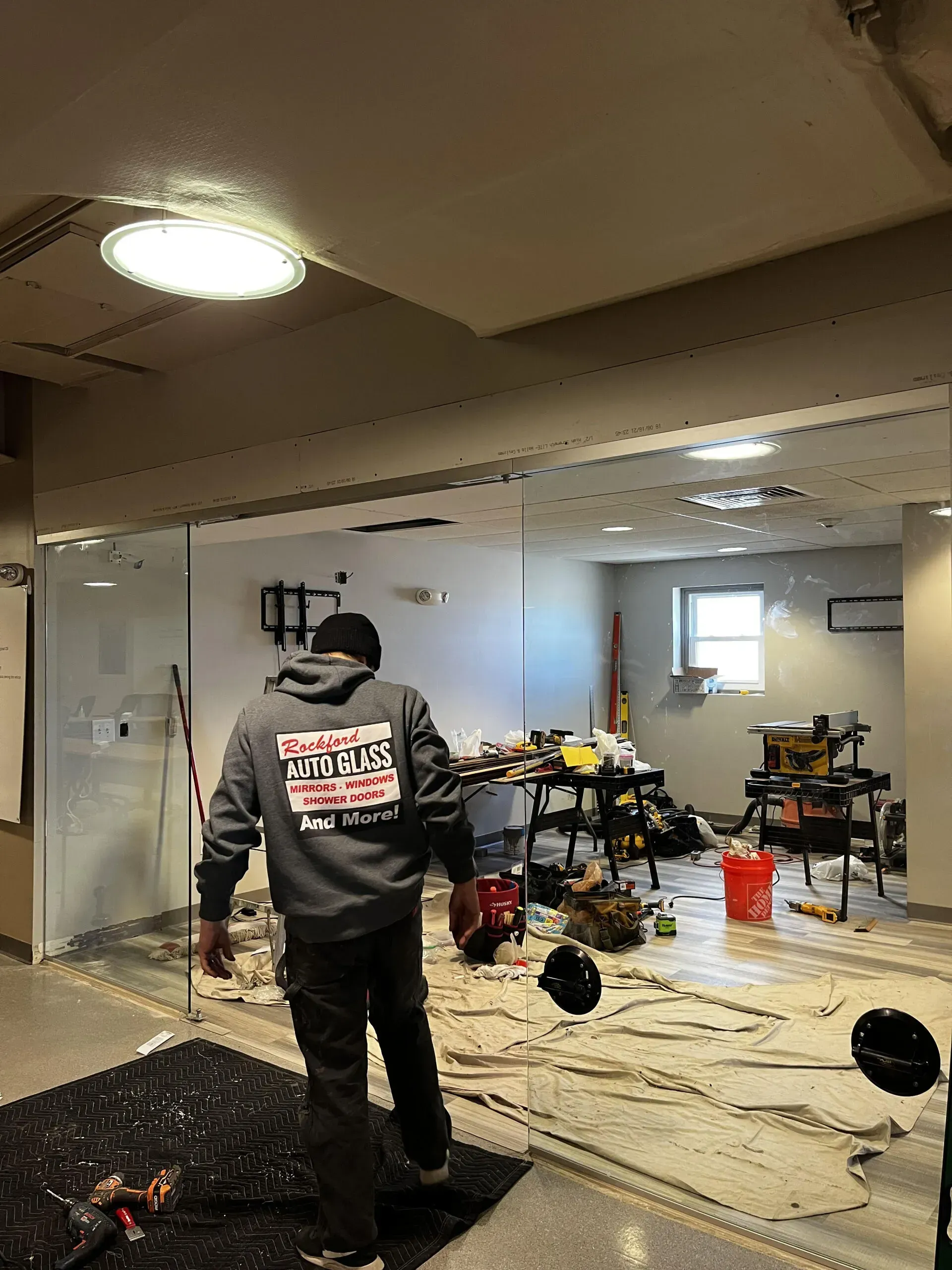 A person in a gray hoodie stands in a room undergoing renovations, with tools and drop cloths scattered across the floor.